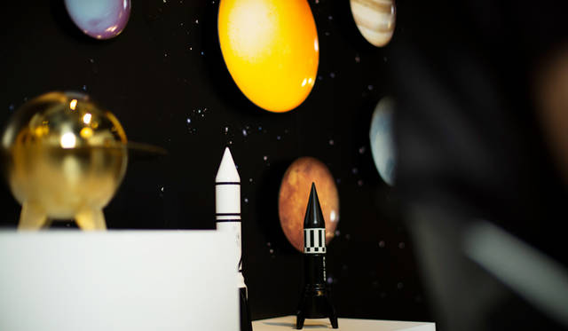 手前のロケット形のオブジェは、ソルト＆ペッパーミル。1970年代に活躍したロケットのグラフィック、カラー、質感からインスパイアされている。背景に見える9つの惑星と太陽と月をモチーフにしたプレートと組みわせれば、宇宙空間にいるかのような世界がひろがる