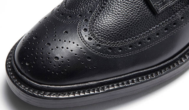 ウイング部分と足入れ周りのスムースキップは、ガラス玉で表面を磨くことでキメ細かくなり、黒みも増すグレイジング加工を採用。グレインドキップはクラシックな小石状の型押しが施されている。遠目は通常の黒靴だが、近づくと表情が現れるユニークなコンビだ。