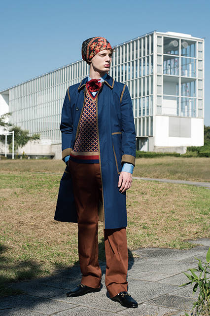 ブラウンのラインをアクセントに効かせたコートは、リバーシブル仕様。インナーにはジャカードのニットを合わせ、胸元にはフラワーモチーフのコサージュを。コートとパンツのゆるやかなシルエットによって、新しいレトロ感が醸し出されている。<br><br>コート30万6720円、パンツ8万5320円、ニット9万9360円、シャツ4万8600円、バンダナ3万1320円、タイ5万2920円、シューズ9万1800円／グッチ＜阪急メンズ大阪2階＞＜阪急メンズ東京2階＞