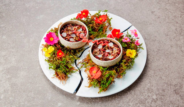 <strong>結び／アミューズ</strong><br>二人で一つである夫婦を二皿で一皿で見えるようなお皿で表現。縁取られたゆるやかな曲線は、夫婦の間に流れる悠久の時間を表している。それぞれのお皿には、菊芋でつくったシロップと、干し草のオイルで味付けされた鹿のタルタル。その上に敷き詰められた葉は、ハートにも見える。夫婦の特別な夜を祝福するかのような華やかな花びらと、二人を結ぶ“赤い糸”をイメージしたビーツのチップスがお皿を繋ぎ、一つの作品となる料理。