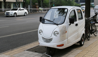 キャビン付き3輪バイクの向こうをインフィニティが通過する